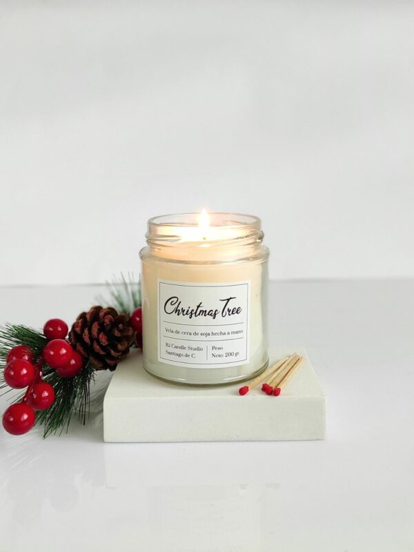 Vela de soja navideña, encendida de estilo minimalista con unas cerillas al lado y un adorno navideño al otro lado.
