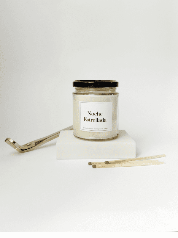 Ambiente minimalista con vela aromática Noche Estrellada encendida, cerillas y un cortamechas en la parte de atrás.