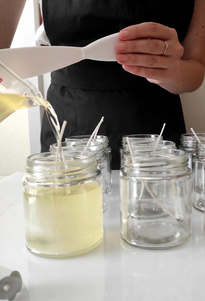 Una persona vertiendo cera en tarros de vidrio