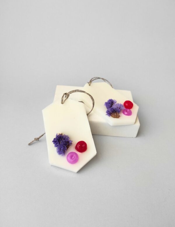 dos ambientadores sólidos colocados sobre un soporte. Están decorados con una flor seca de color violeta y dos bolitas de cera una roja y otra de color rojo. Aroma a Clean Cotton