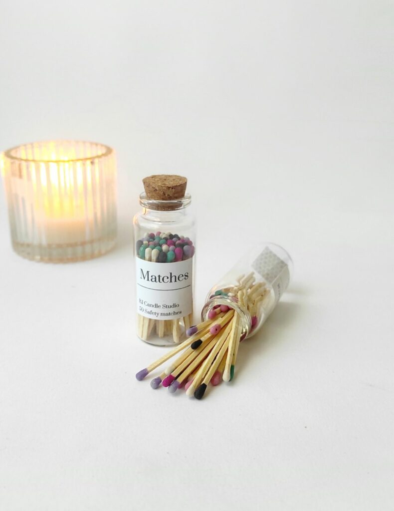 Cerillas de colores desparramadas desde un bote abierto, al lado otro cerrado y al fondo una vela encendida