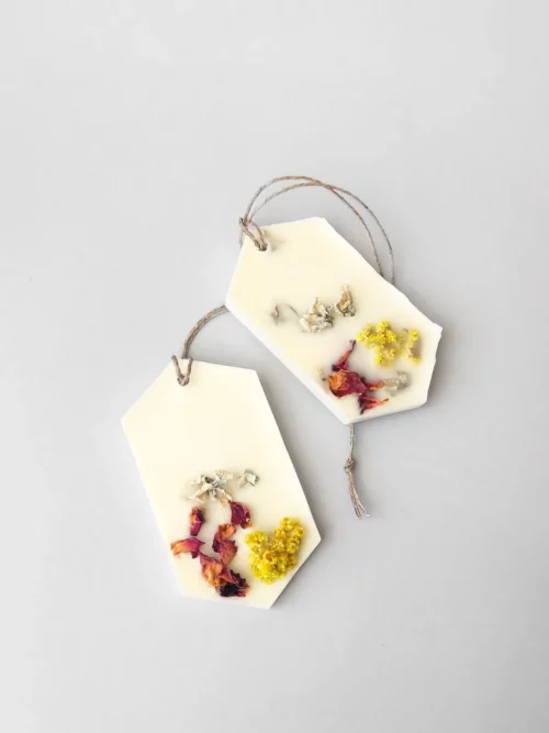 Dos ambientadores sobre fondo gris. Están decorados con flores secas y pétalos de rosa