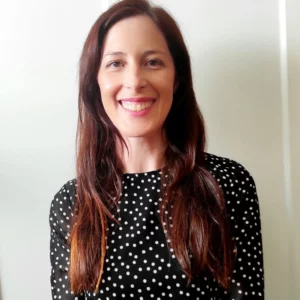 Imagen en la que se ve a Elena sonriente, quien es la creadora de BJ Candle Studio. Tiene el pelo largo y castaño y lleva una blusa negra con lunares blancos.