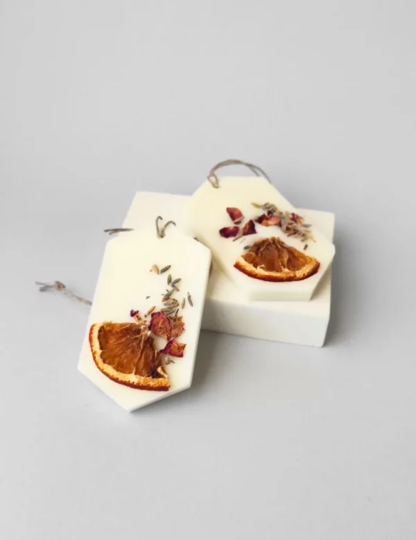 dos ambientadores sólidos decorados con un trozo de naranja deshidratada, semillas de lavanda y pétalos secos de rosa