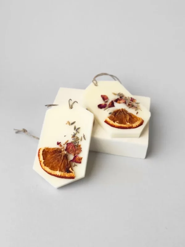 dos ambientadores sólidos decorados con un trozo de naranja deshidratada, semillas de lavanda y pétalos secos de rosa