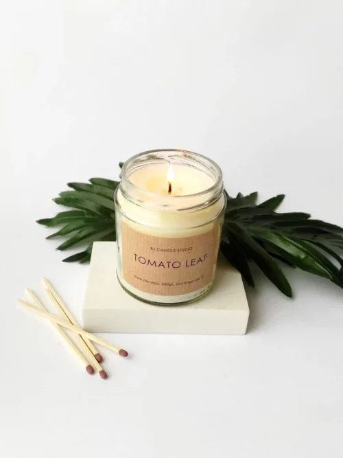 Vela aromática hecha a mano, encendida. La escena se completa con hojas de decoración y cerillas.