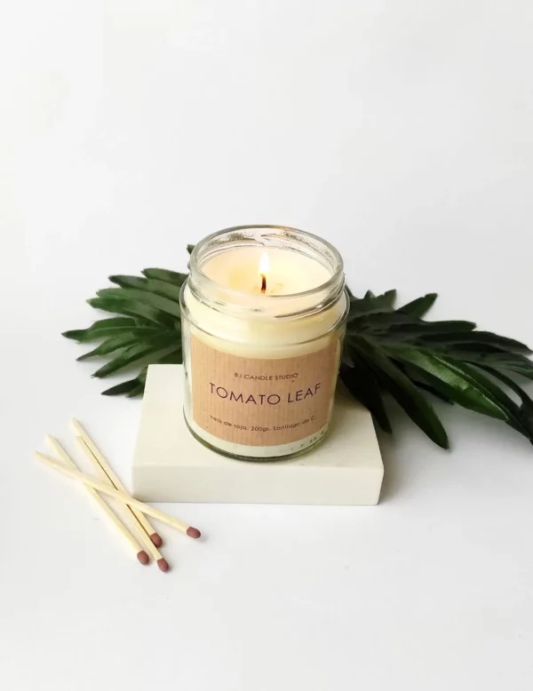 Vela aromática hecha a mano, encendida. La escena se completa con hojas de decoración y cerillas.