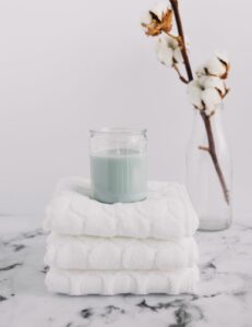 vela en tono verde pastel sobre unas toallas dobladas y una rama de algodón al fondo