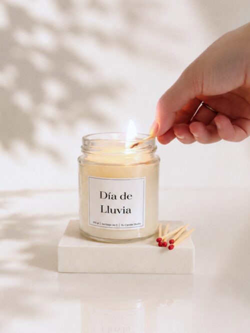Una mano encendiendo la vela aromática Día de Lluvia con una cerilla. Estilo minimalista.